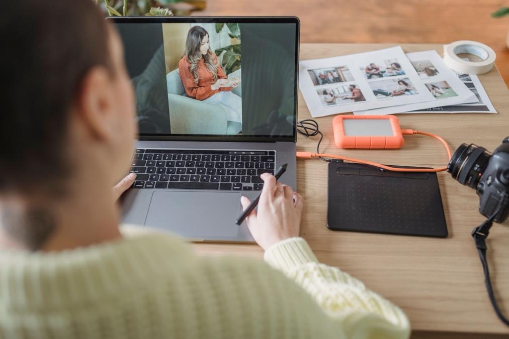 A person working at a laptop with a recorded video interview playing on the screen